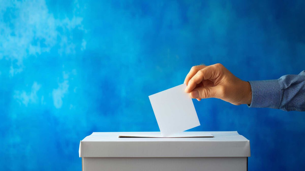 Hand dropping a blank ballot into a voting box on a blue background